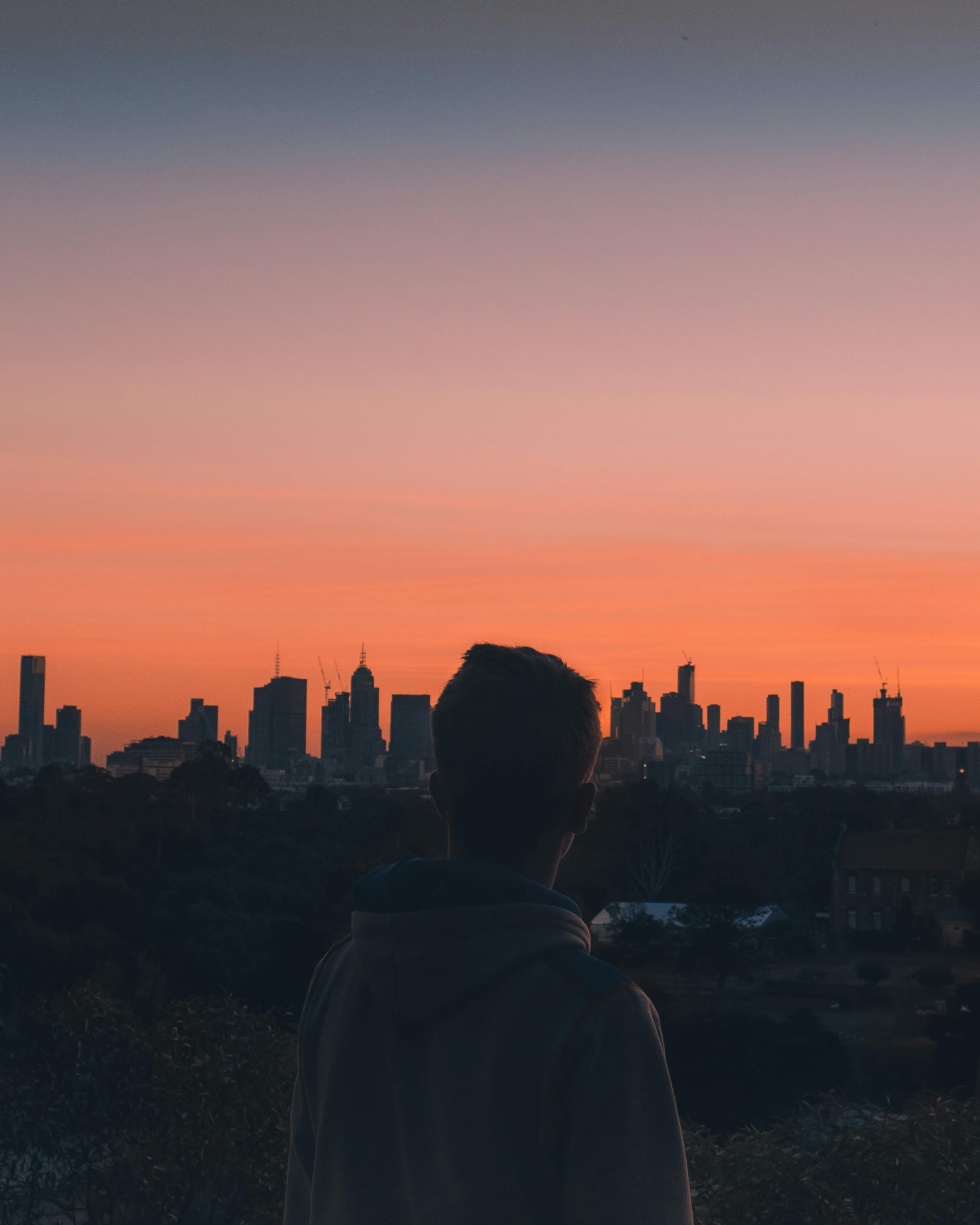 A Man Standing Looking at a Cityscape during Sunset